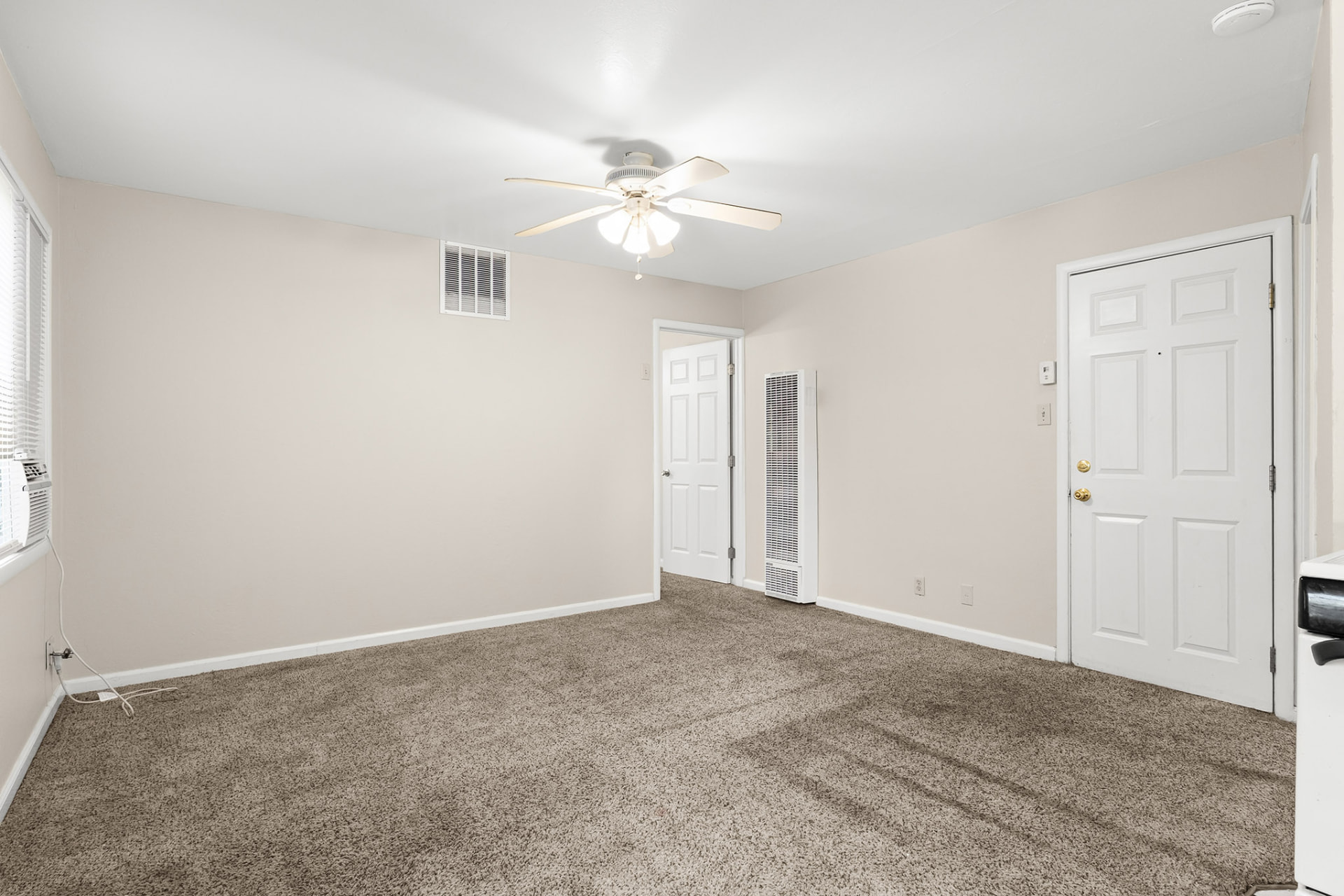 Carpeted living room with ceiling fan and entry door in a Magnolia Apartments unit