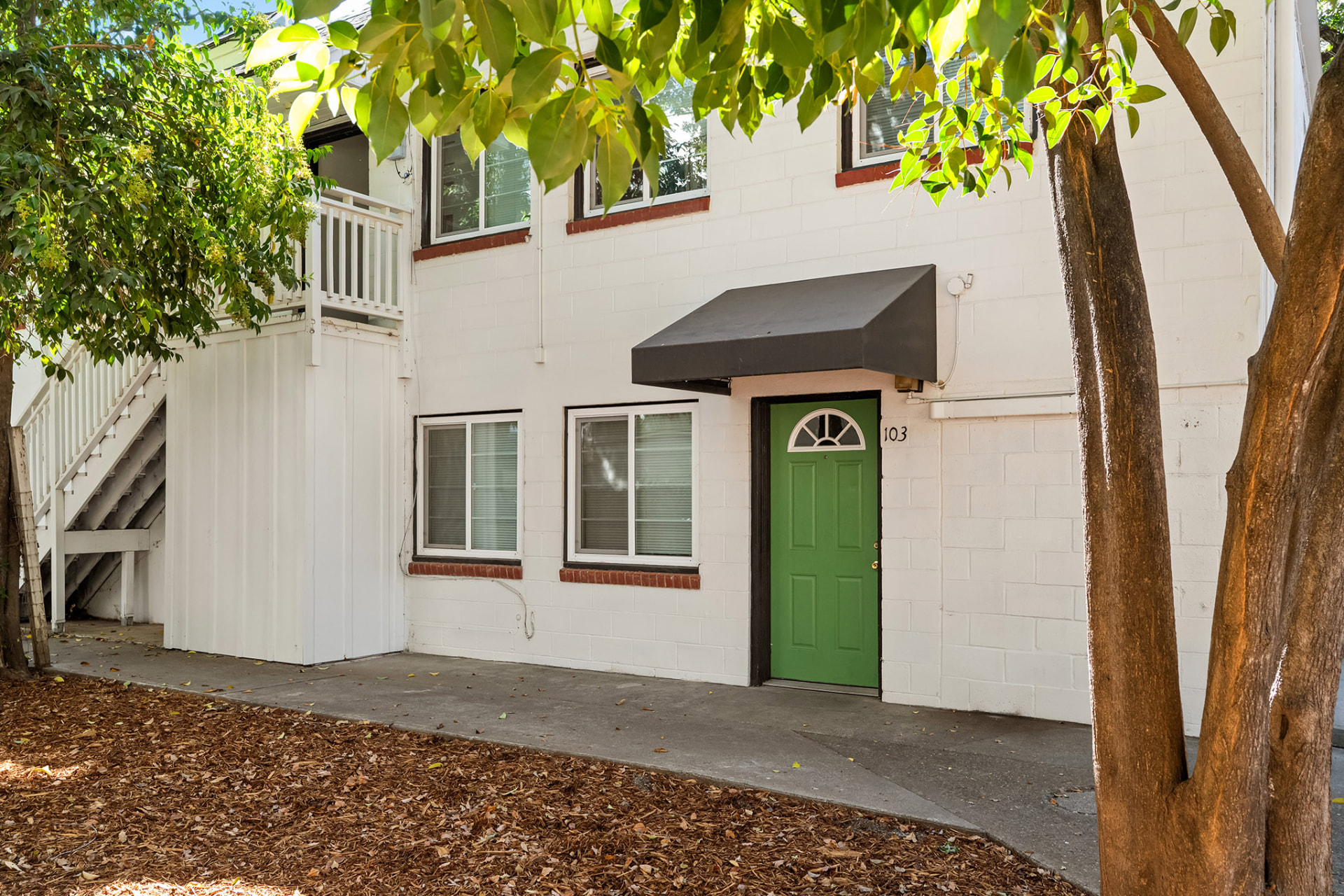 Ground-floor unit entry with green door and awning on the white brick building