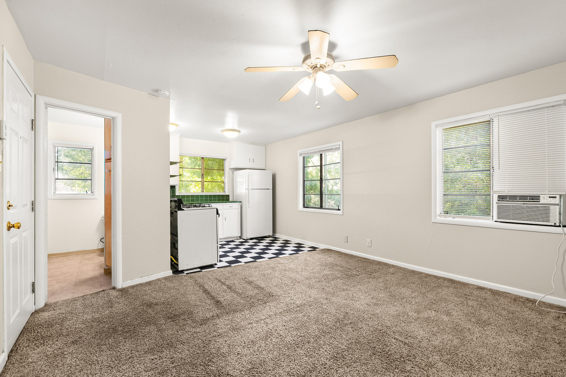 Open living area with adjoining kitchen, ceiling fan, and multiple windows
